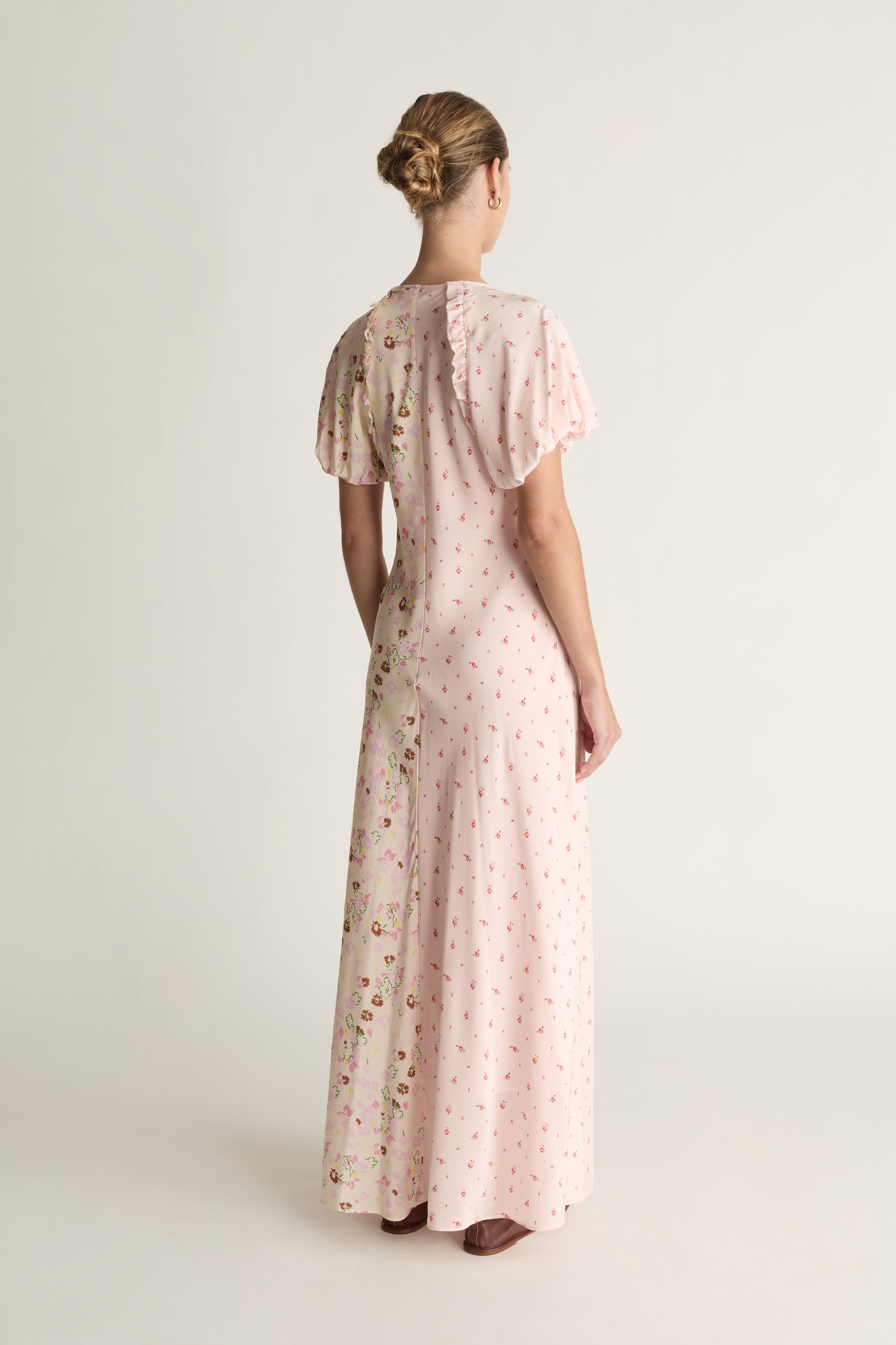 Woman wearing a long, light pink dress with floral pattern on a white background