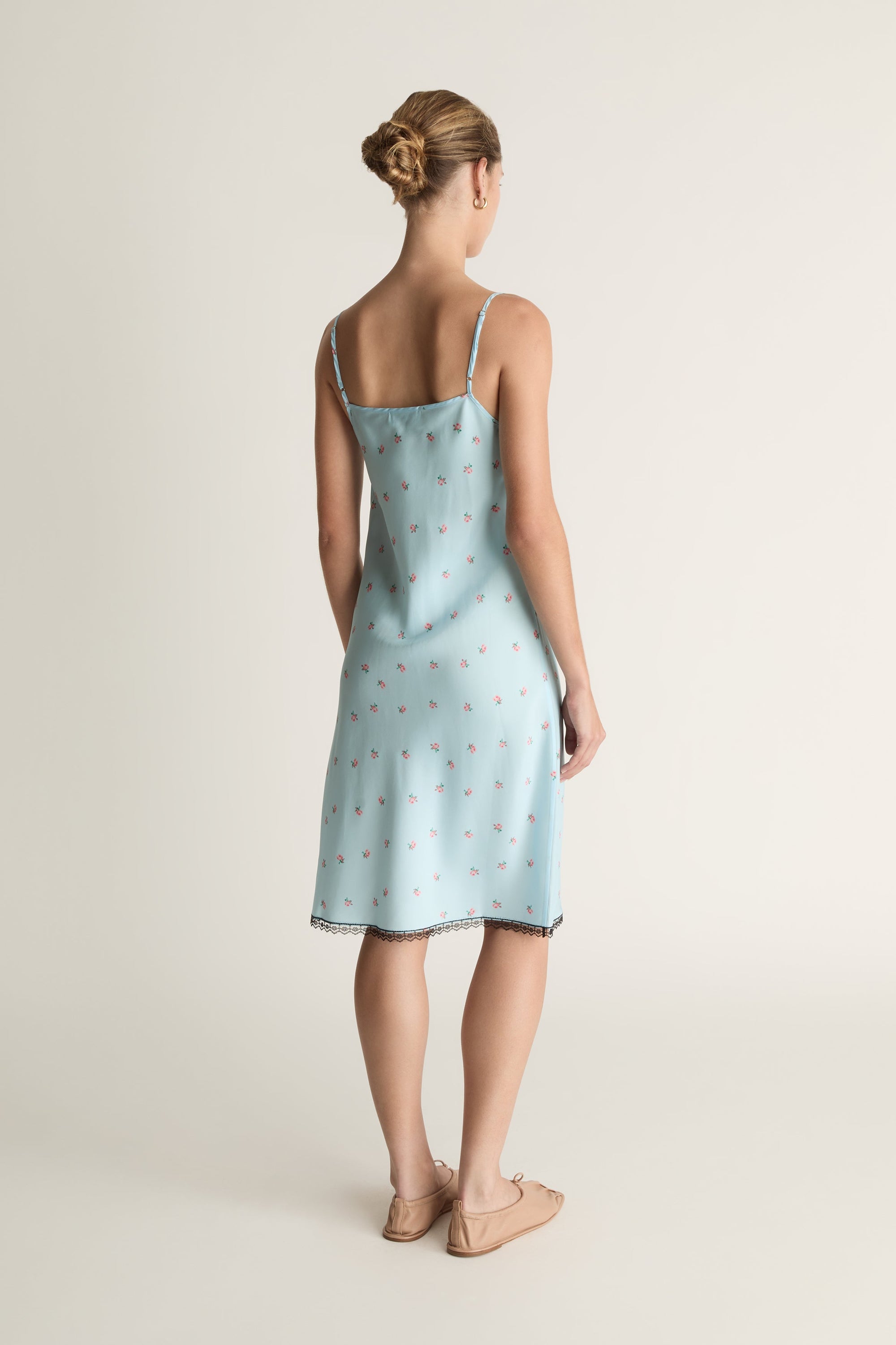 Woman wearing a light blue slip dress with a subtle pattern on a plain background
