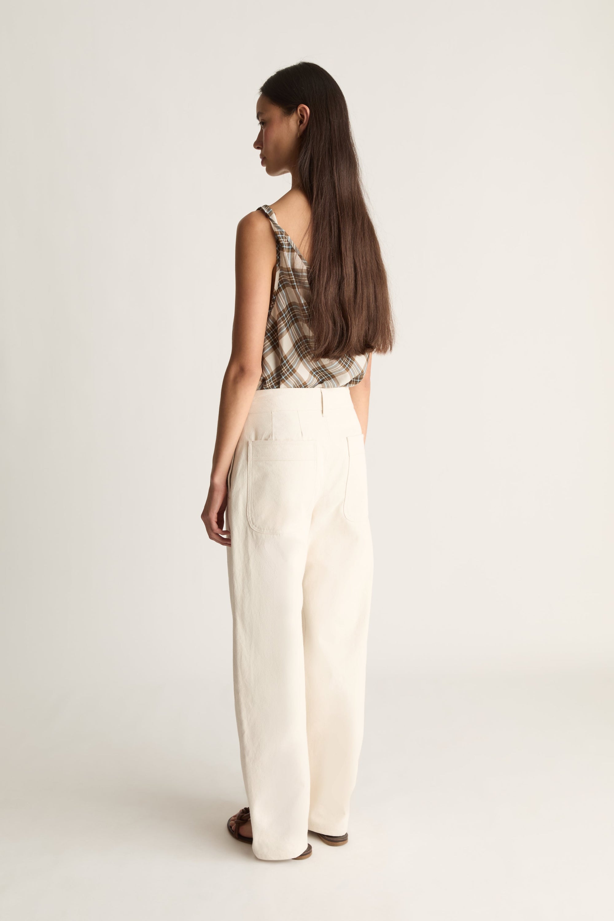 A woman shown from the back wearing a sleeveless plaid top and wide-leg cream canvas trousers against a plain light background.