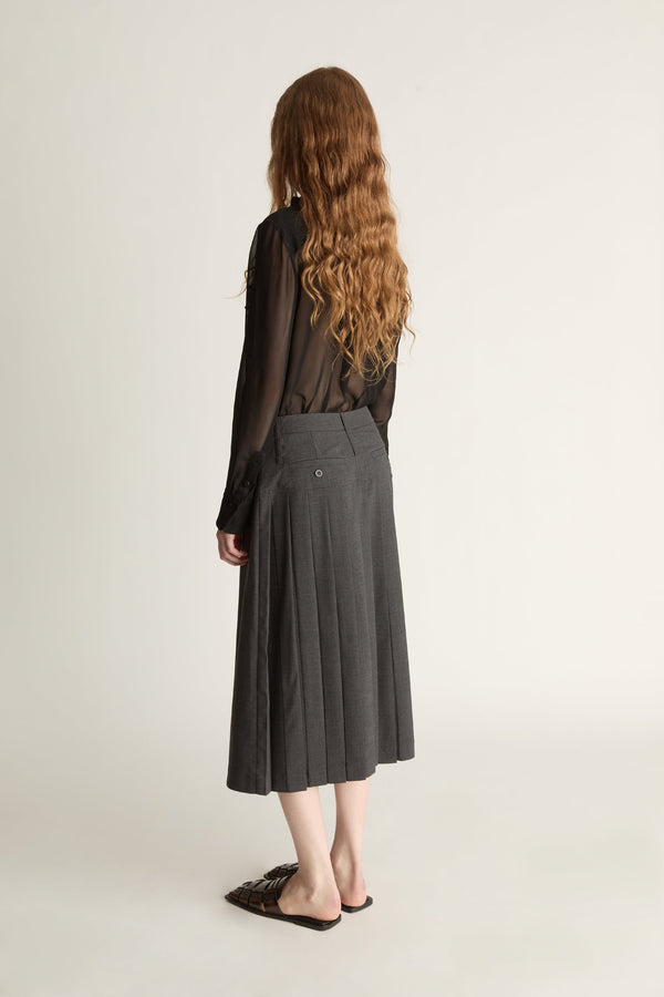 Person wearing a black blouse with lace details and a gray pleated skirt on a white background