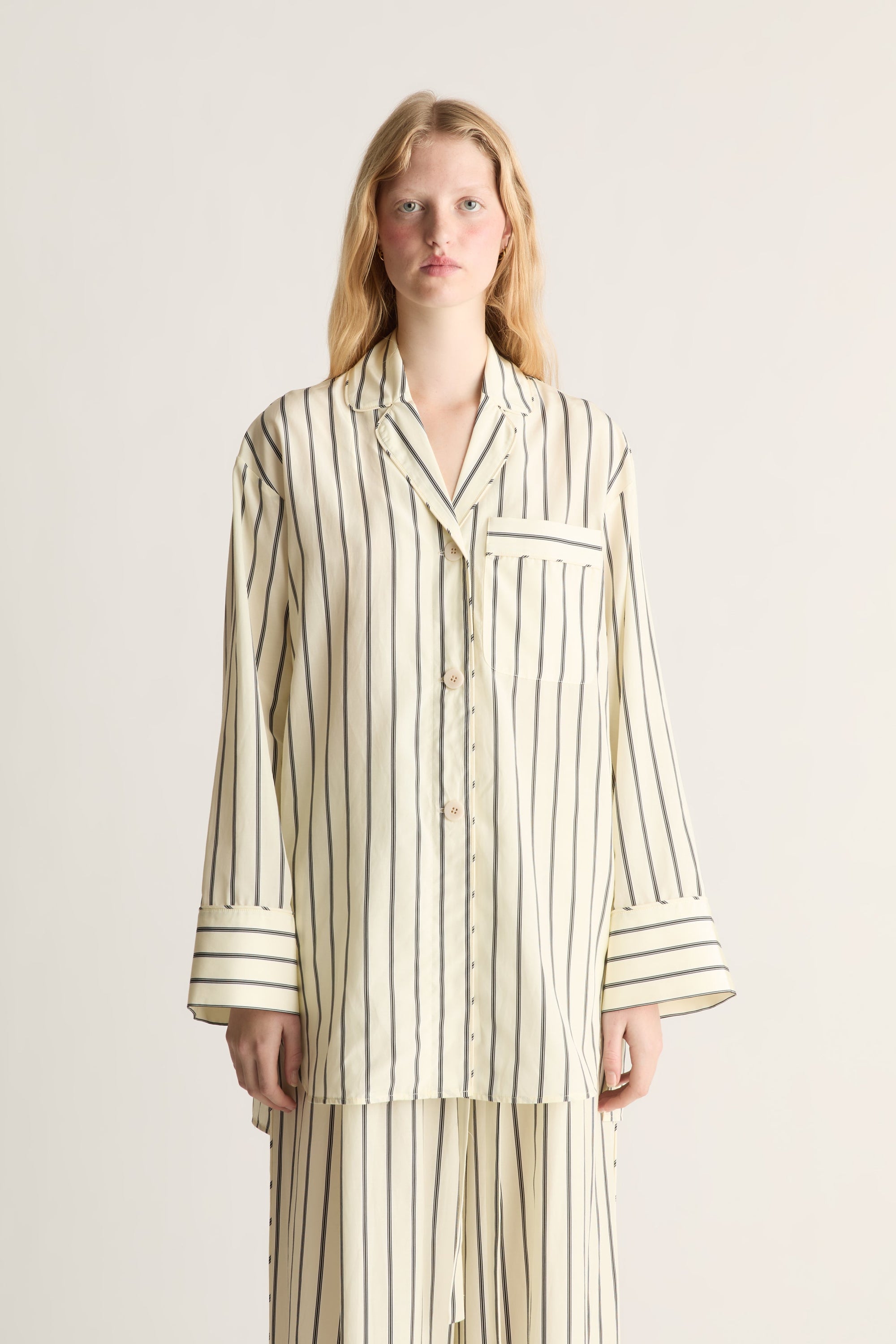 Close up of a woman wearing a lemon yellow and black stripe pyjama-style shirt and trousers on a white background
