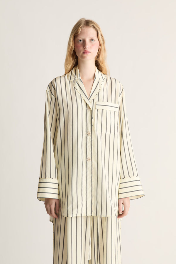 Close up of a woman wearing a lemon yellow and black stripe pyjama-style shirt and trousers on a white background