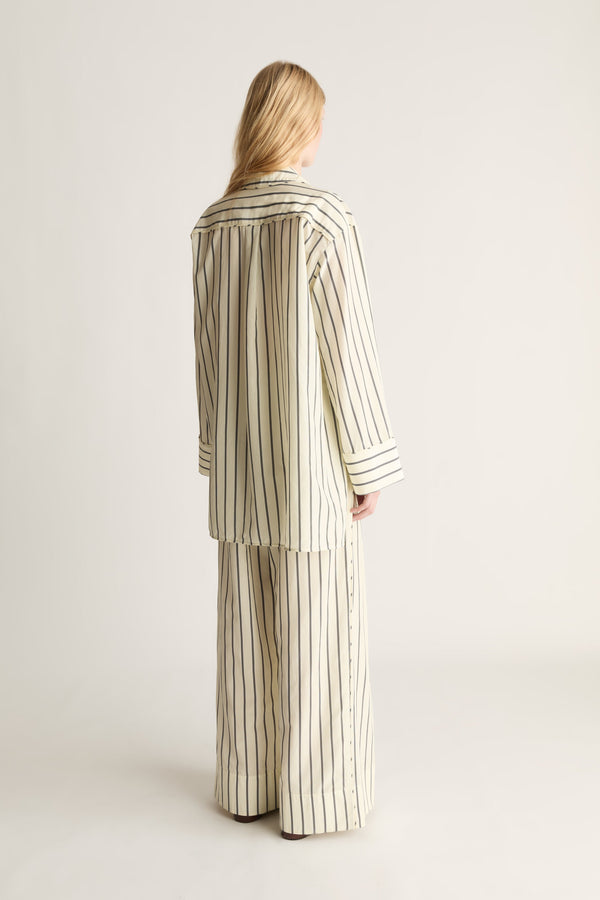 Back view of a woman wearing a lemon yellow and black striped shirt and trousers on a white background.