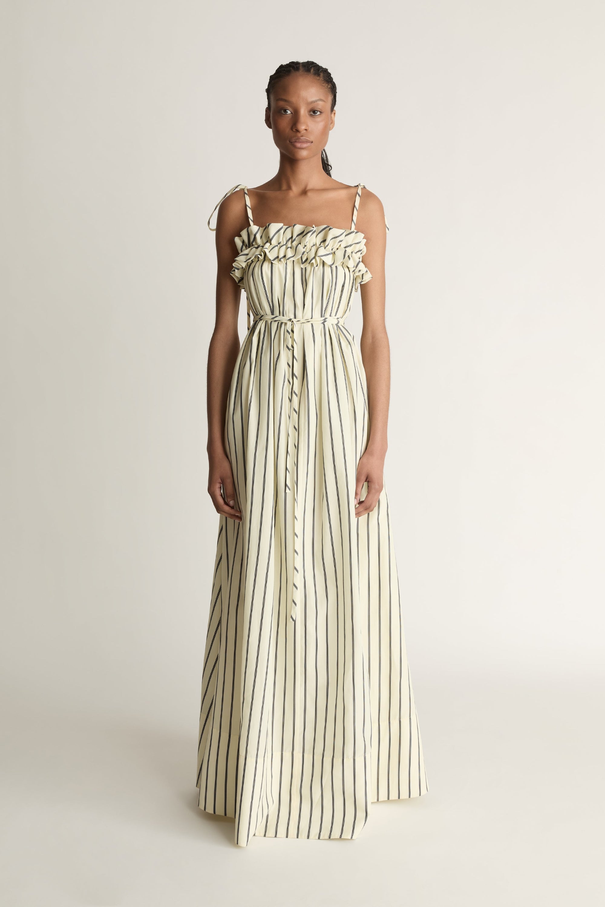 Front view of a woman wearing a full-length yellow and black stripe dress with a frill detail on a white background