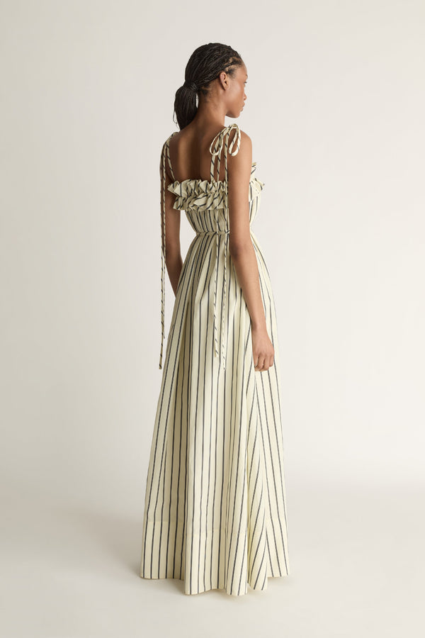 Back view of a woman wearing a full-length lemon yellow and black stripe dress with a waist tie on a white background.