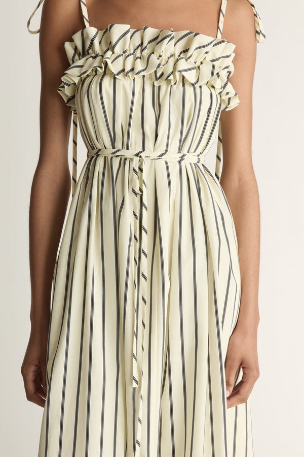Close up of a woman wearing a yellow and black striped dress with a ruffle detail across the bust on a white background