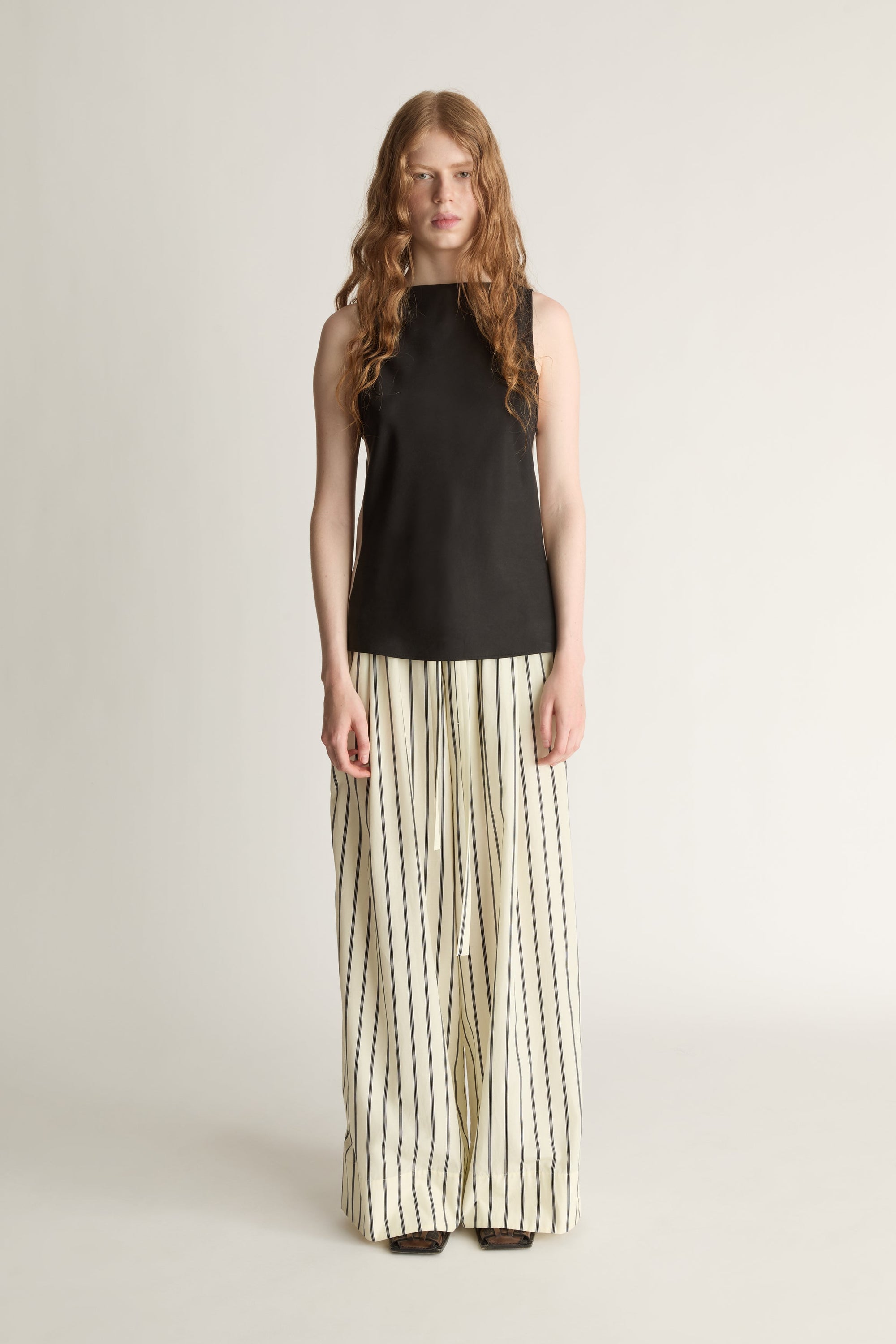 A woman wearing a striped yellow and black pair of wide-leg trousers and a black bias blouse on a white background.
