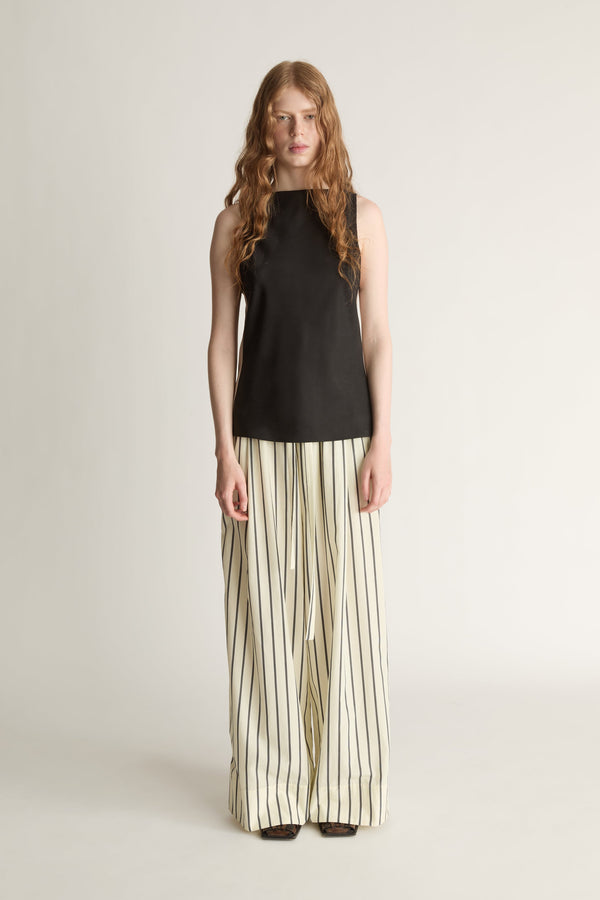 A woman wearing a striped yellow and black pair of wide-leg trousers and a black bias blouse on a white background.