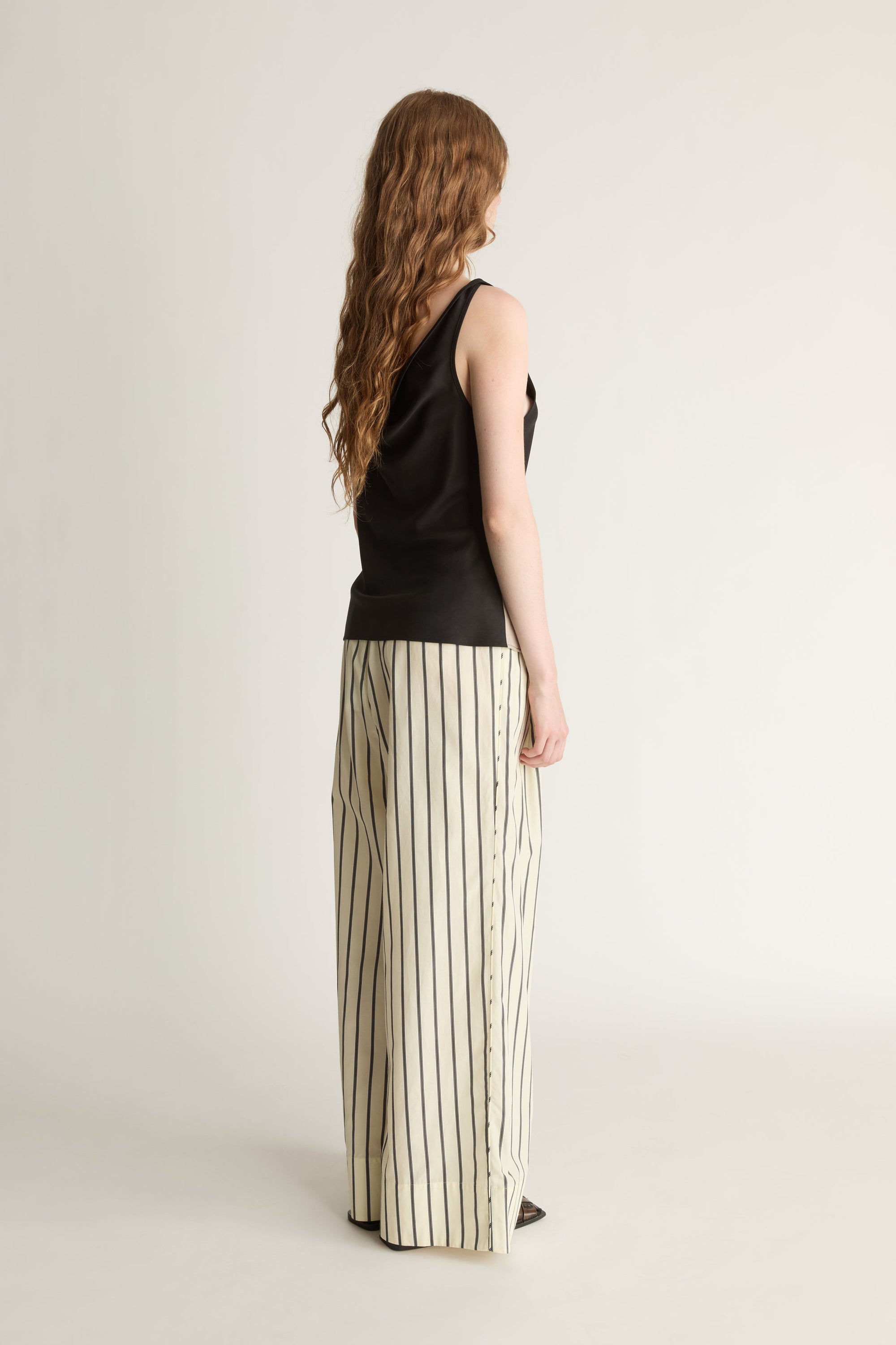 Back view of a woman wearing a pair of yellow and black striped trousers and a black sleeveless top on a white background