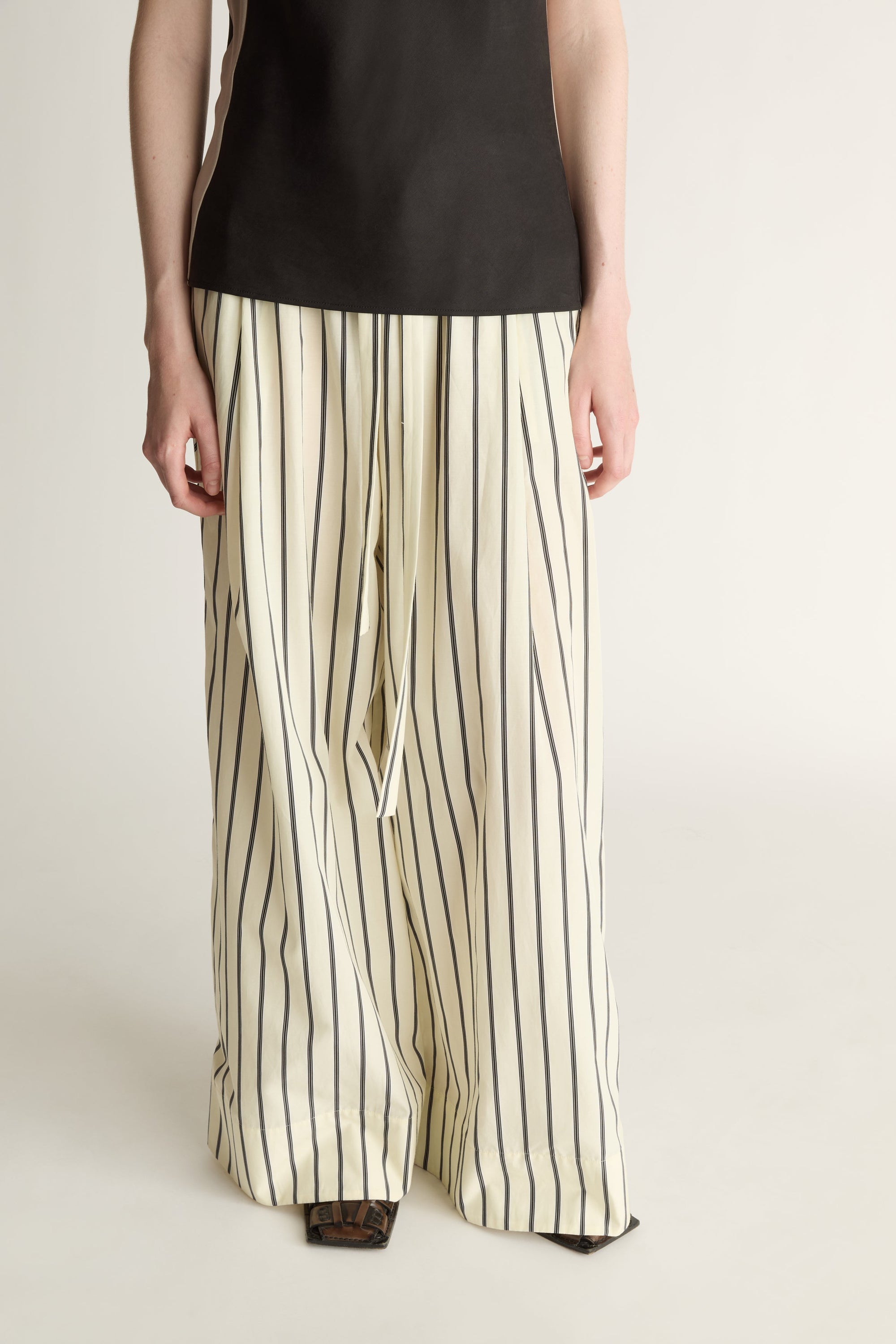 A close-up of a pair of lemon yellow and black striped  drawstring pants on a white background.