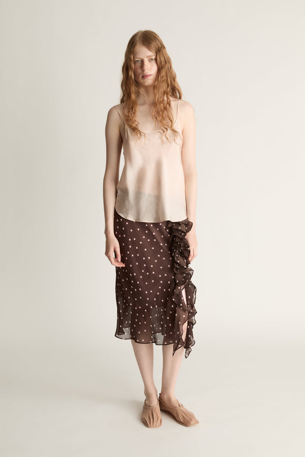 A woman wearing a beige cami top and brown and pink polka dot skirt on a plain background