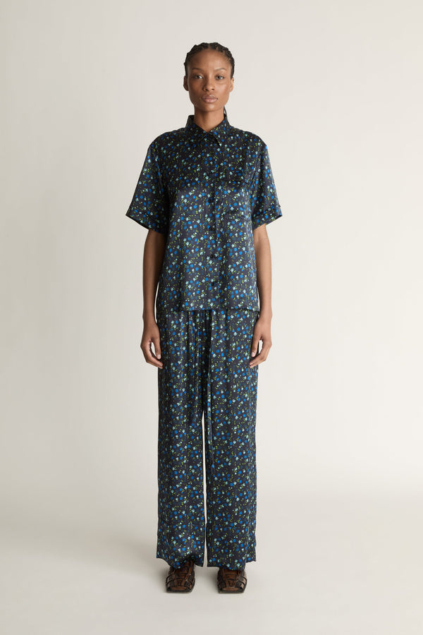 Person wearing a blue printed button-up shirt and pants on a plain background