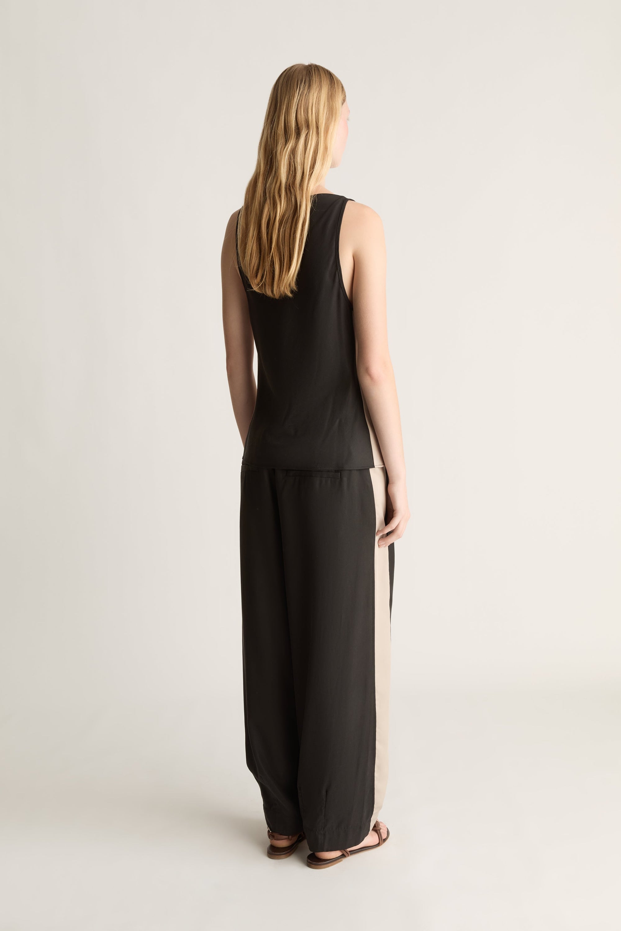 Back view of a woman wearing a black bias tencel blouse and pants on a white background 