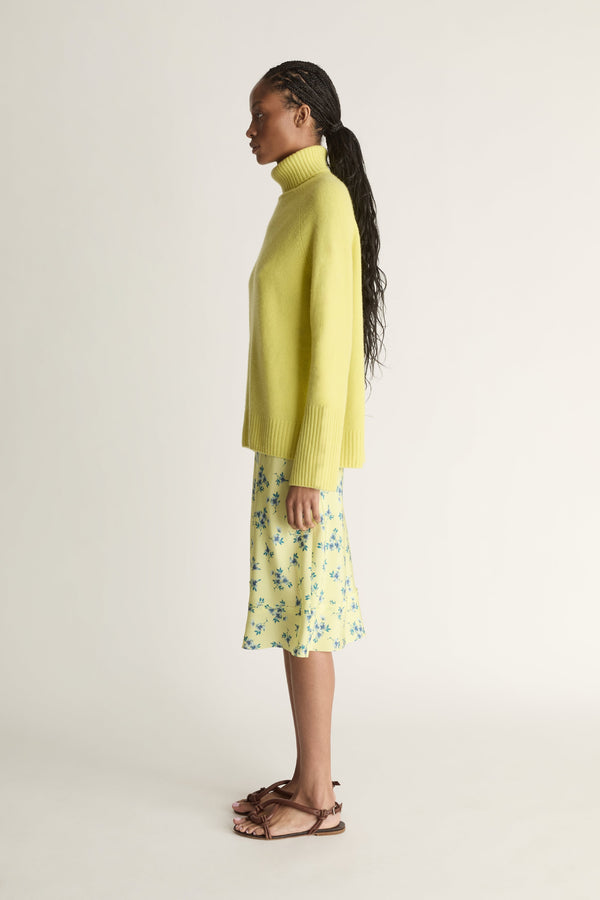 Woman wearing a yellow sweater and floral skirt on a plain background