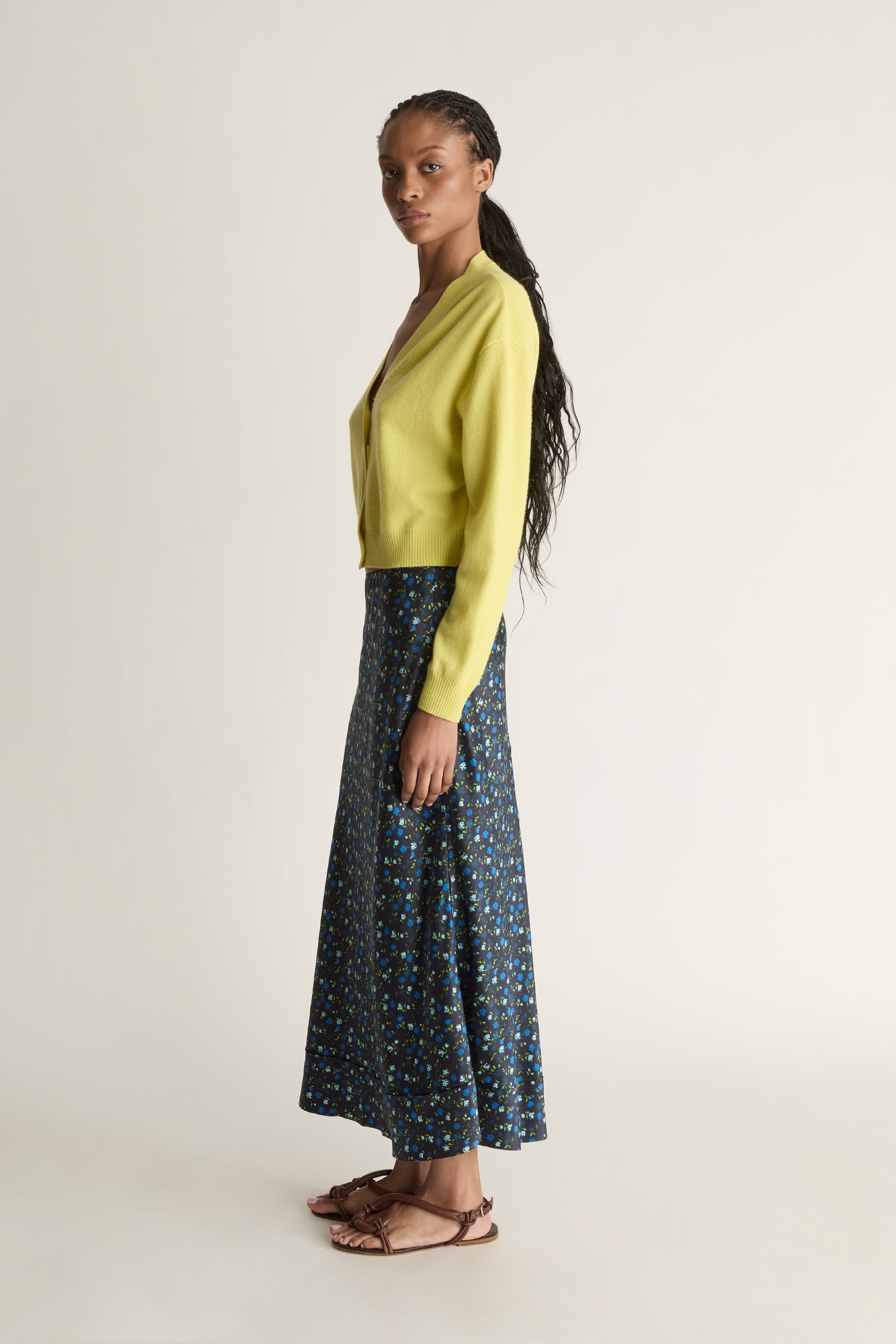 Woman wearing a yellow cardigan and patterned skirt on a white background