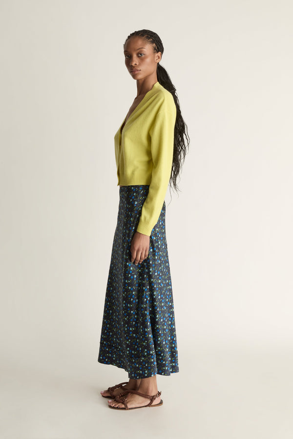 Woman wearing a yellow cardigan and patterned skirt on a white background