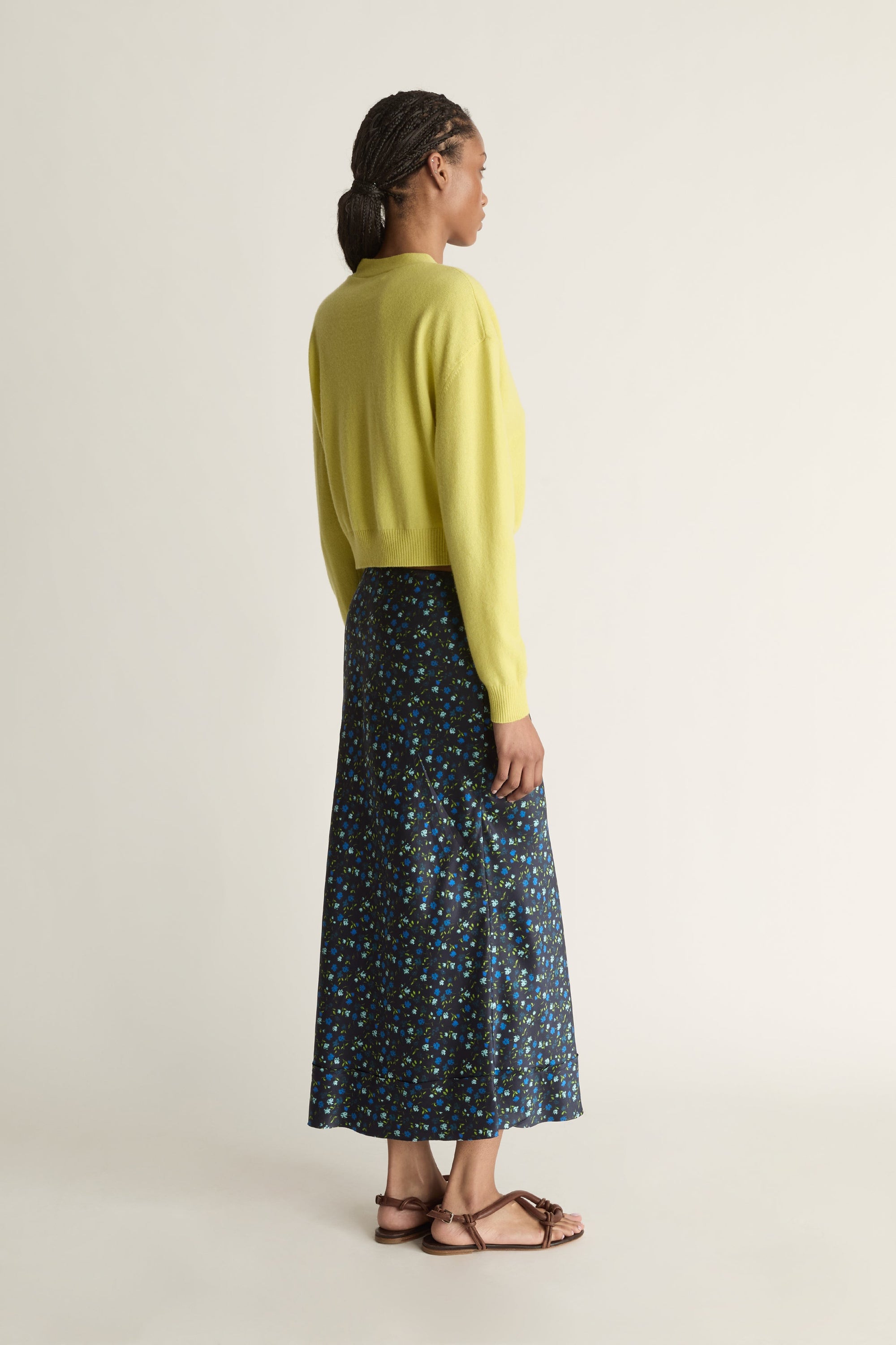 Woman wearing a yellow cardigan and patterned skirt on a white background