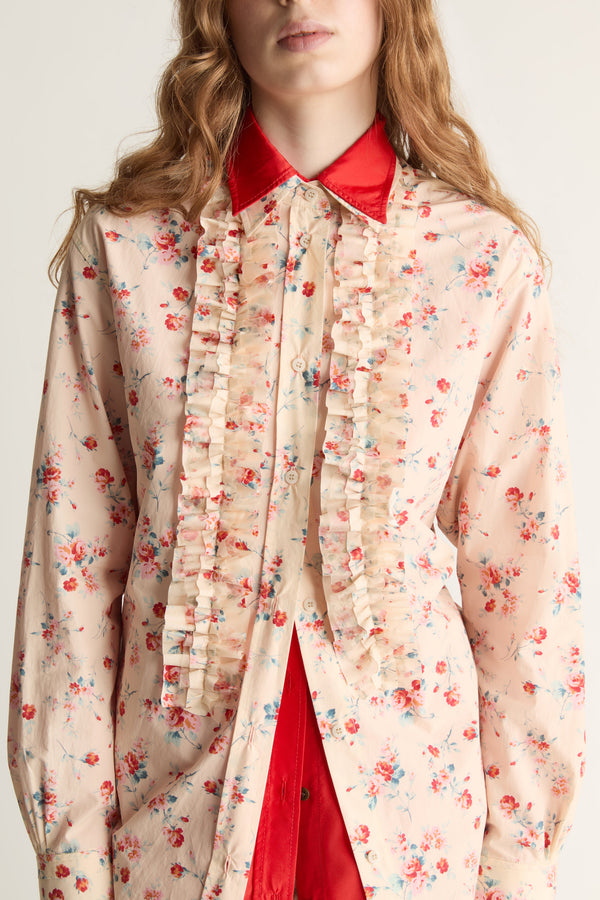 A woman wearing a floral shirt over a red collared shirt against a plain background