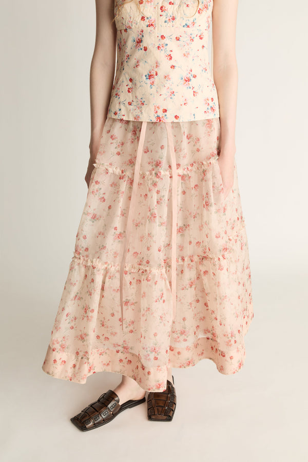 A woman wearing a floral top and skirt on a plain background