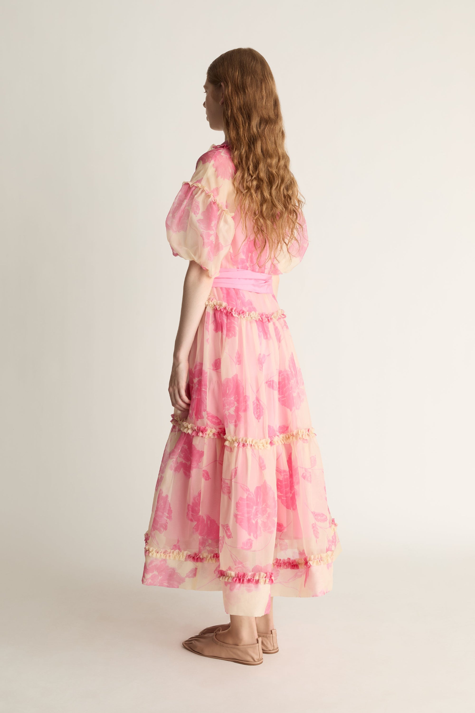 Woman wearing a pink floral dress with sheer sleeves on a white background