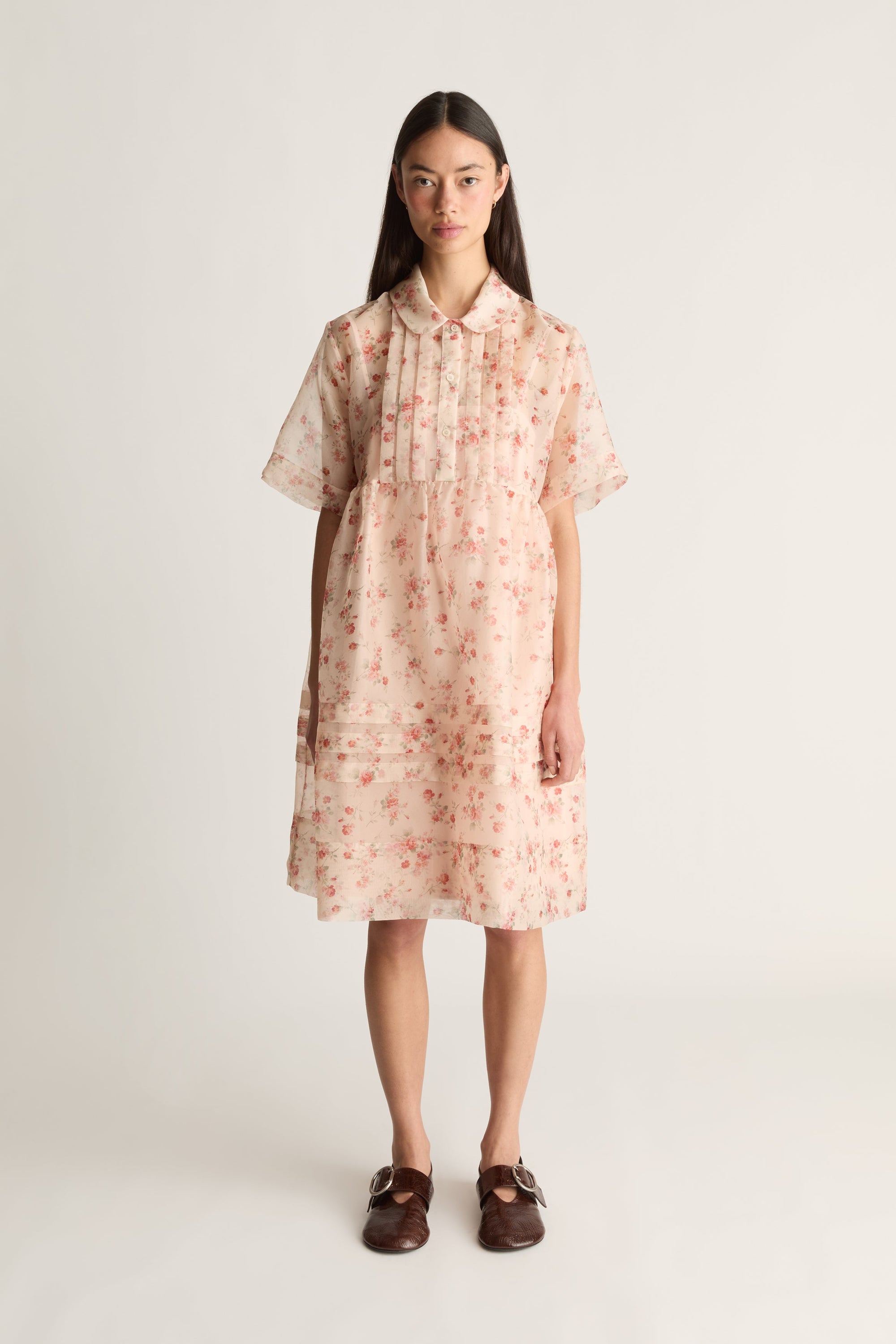 A front view image of a woman wearing a floral mini dress on a white background