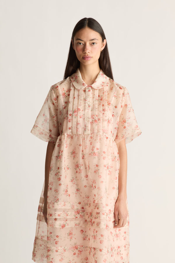 A close up of a woman wearing a floral dress on a plain background
