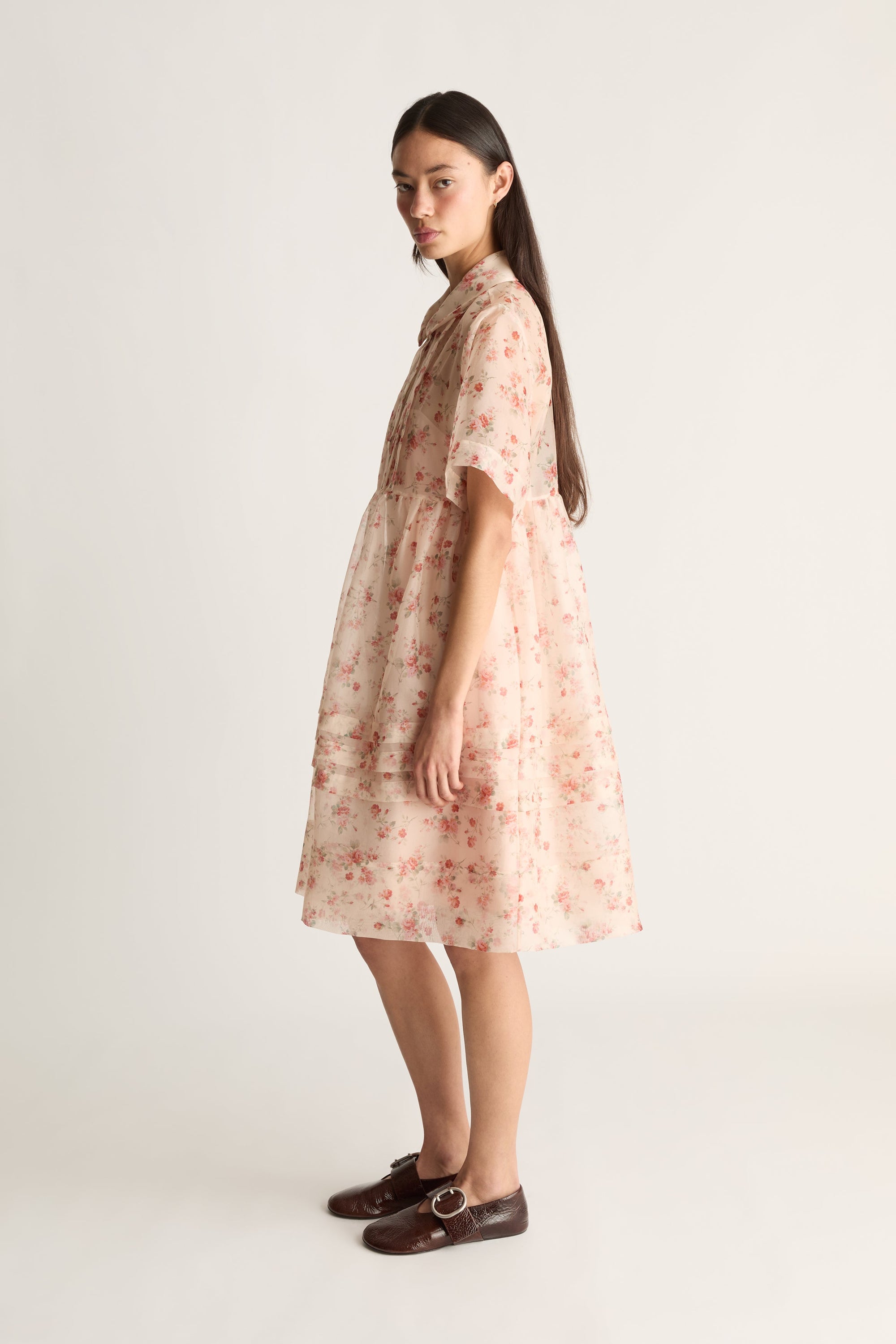 Side view image of a woman wearing a sheer floral mini dress against a white studio background. 