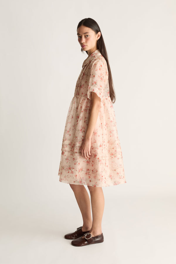Side view image of a woman wearing a sheer floral mini dress against a white studio background. 