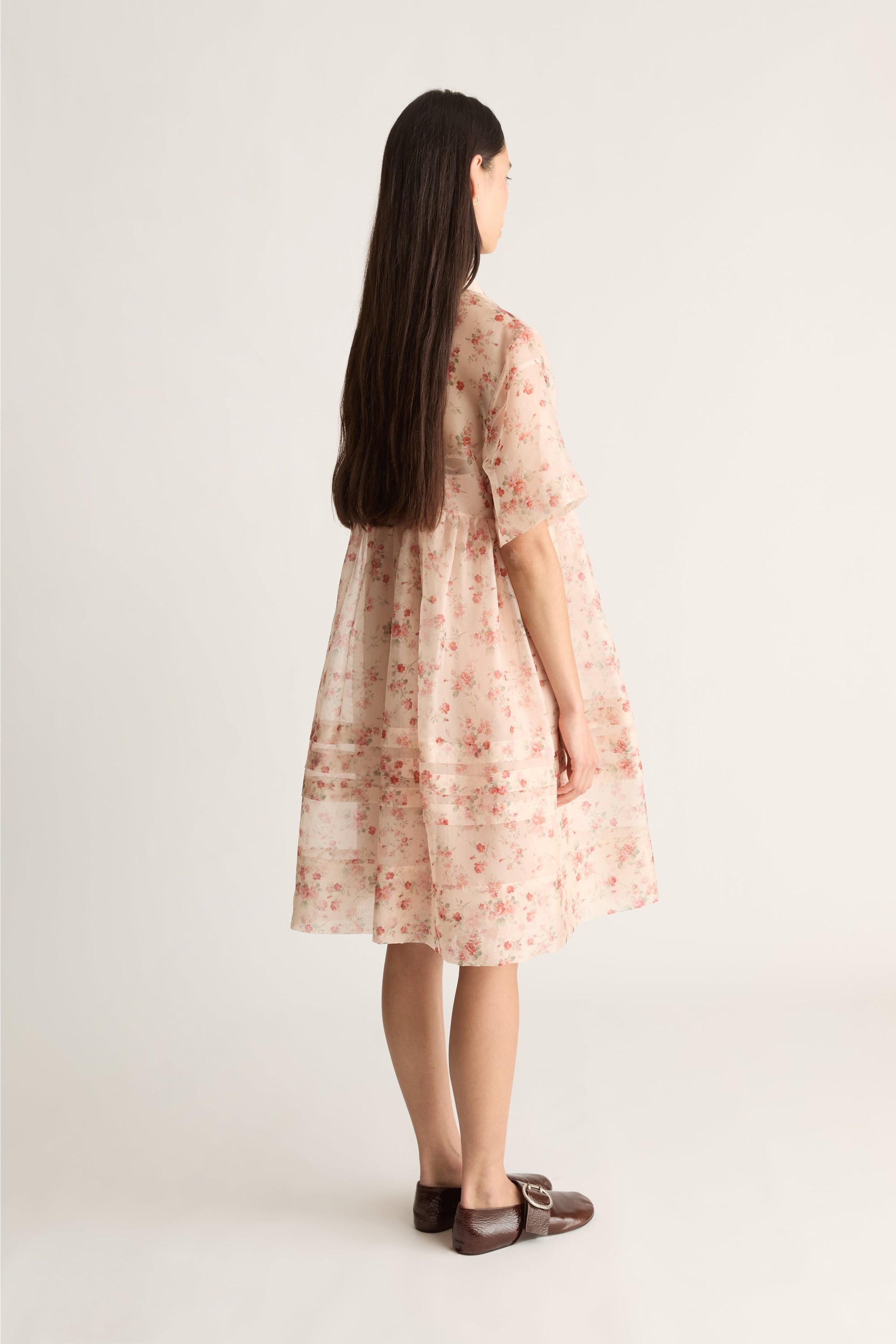 Back view of a woman wearing a floral dress on a white background