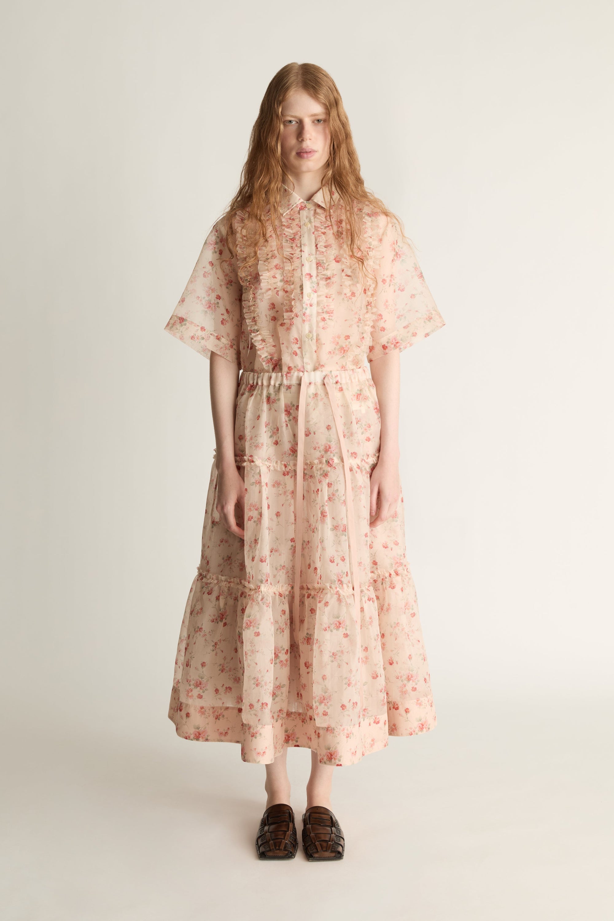A woman wearing a floral shirt and skirt on a plain background