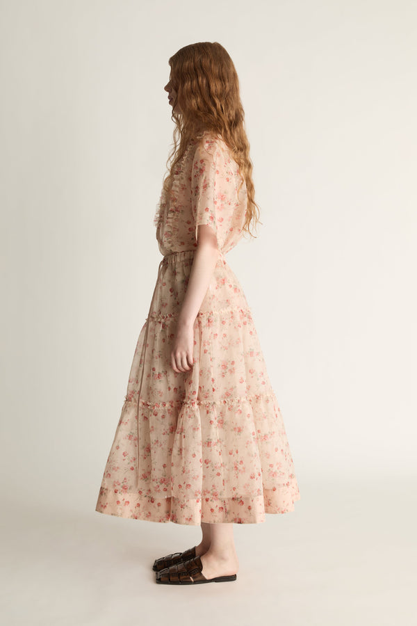 A woman wearing a floral shirt and skirt on a plain background