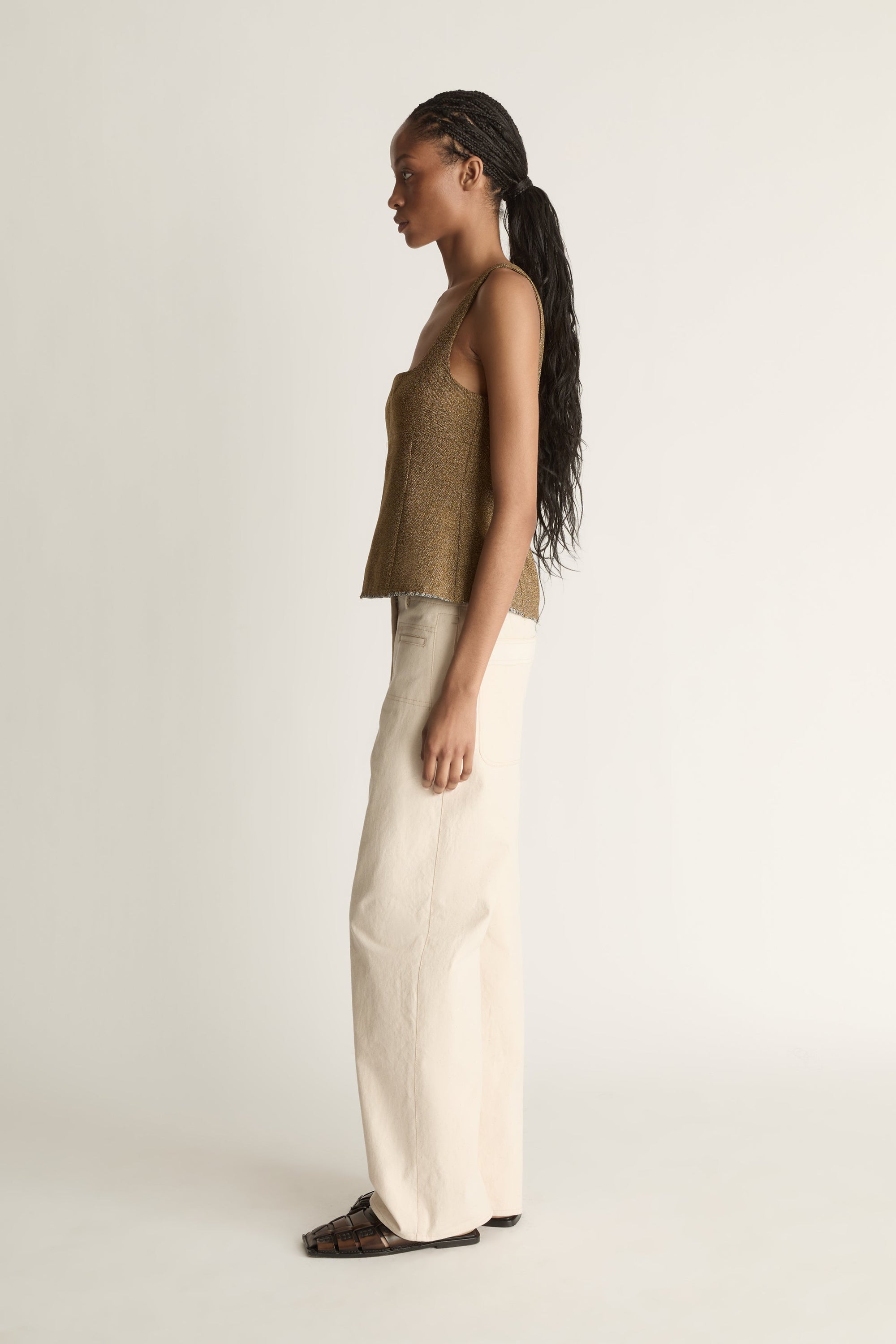 Side view image of a woman wearing a brown wool/linen tank top and a pair of cream jeans on a white background 