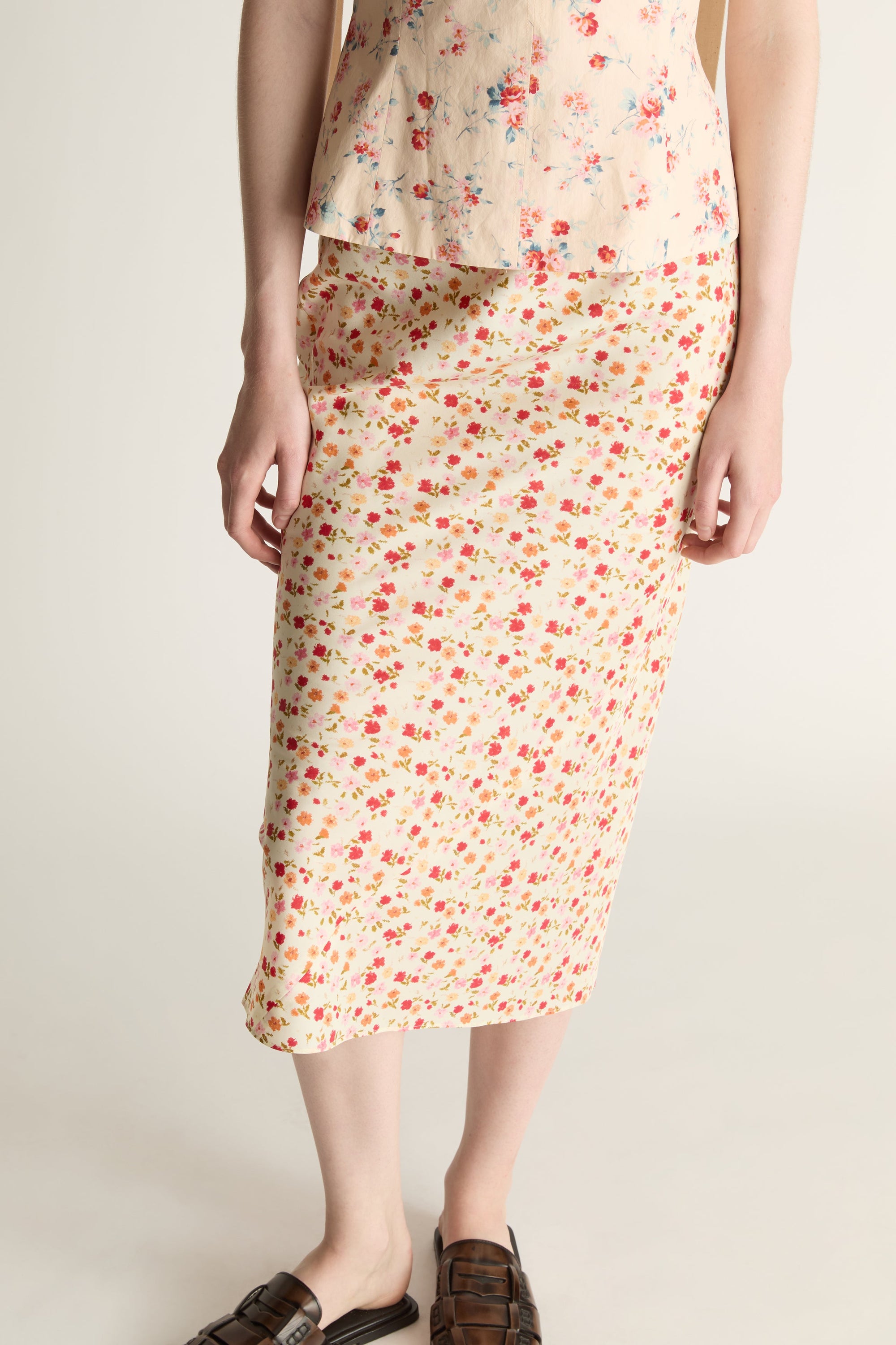 Woman wearing a floral blouse and slip skirt on a plain background