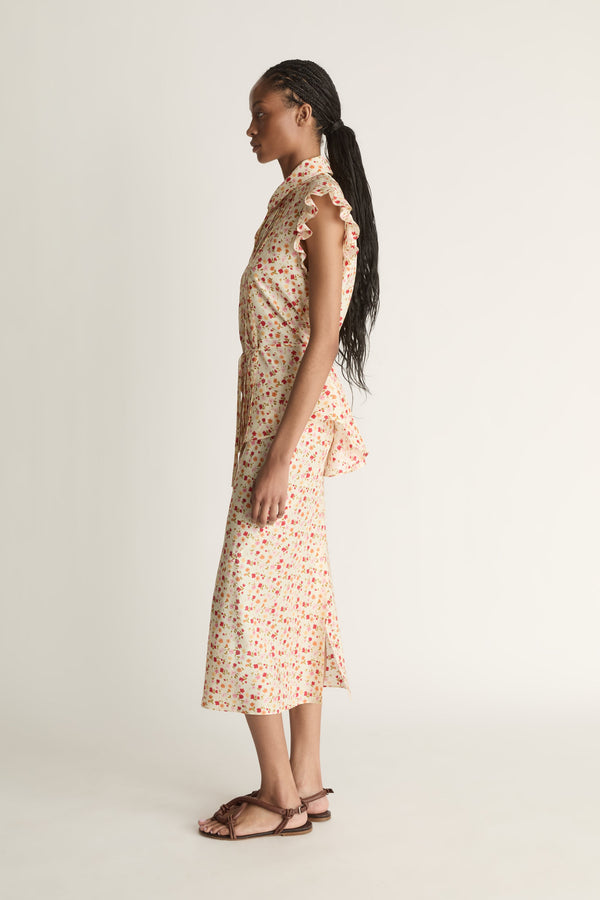 A woman wearing a floral shirt and skirt on a plain background