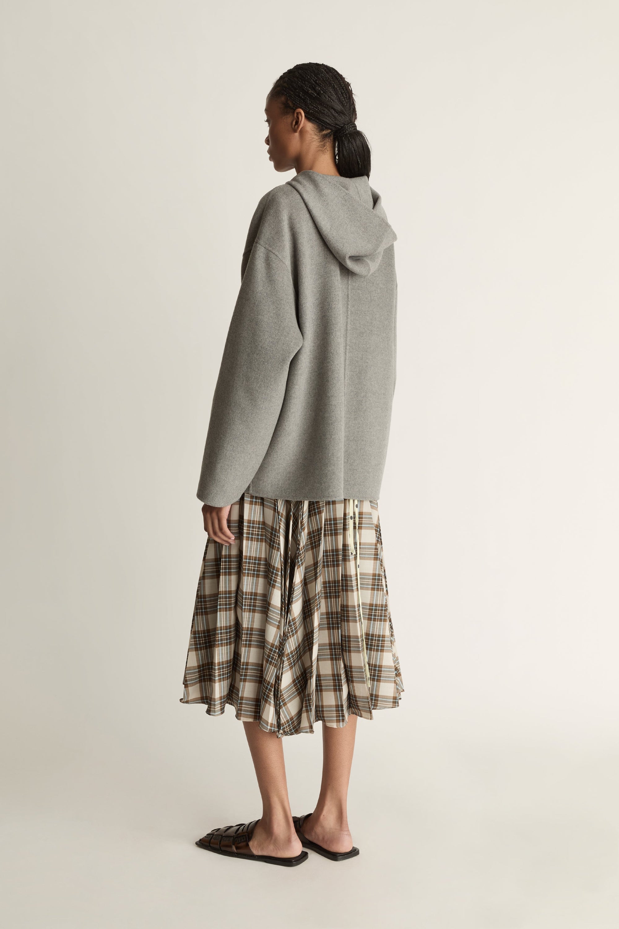 Person wearing a gray hoodie and plaid skirt on a plain background