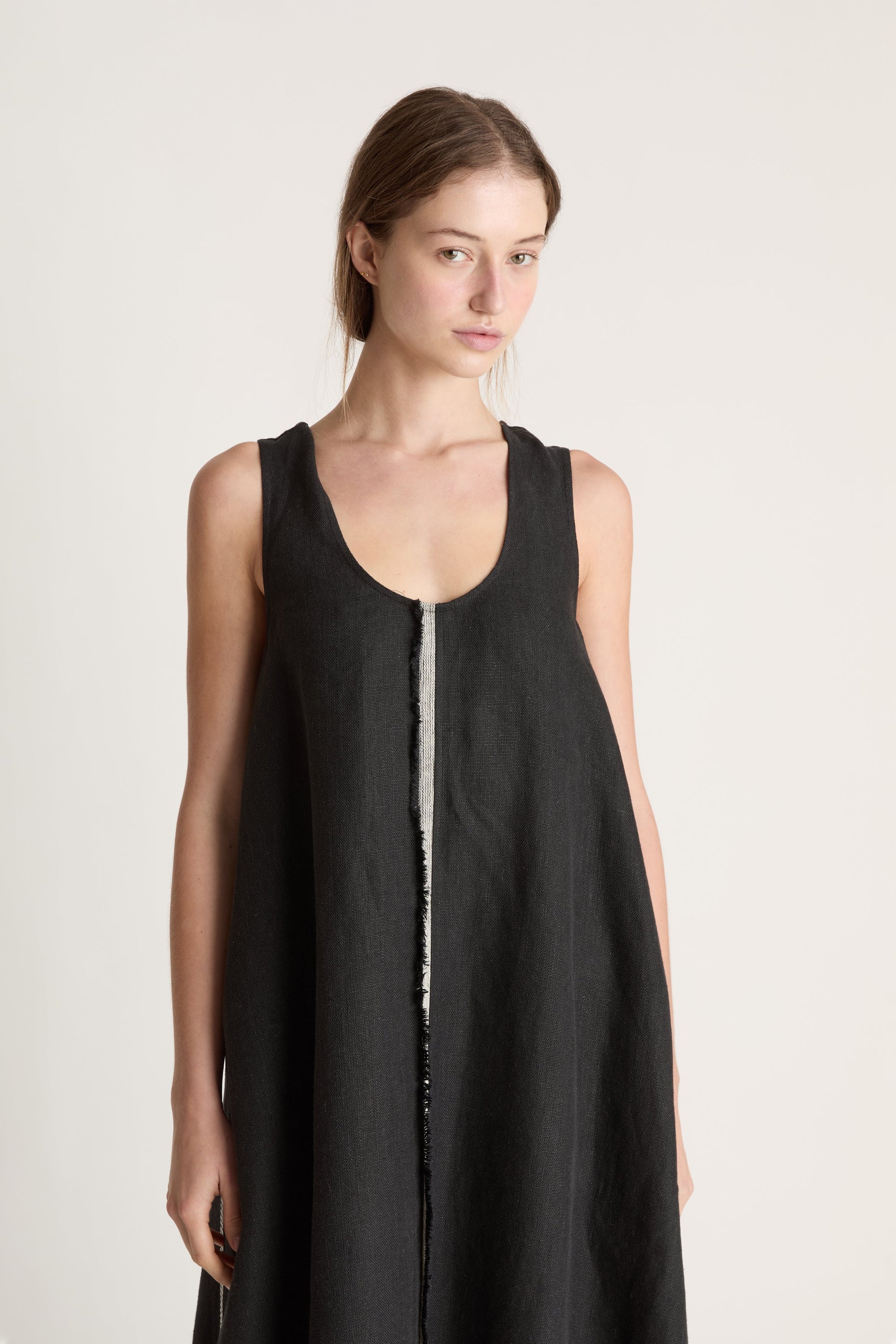 Woman wearing a black sleeveless dress with astripe down the front on a white background