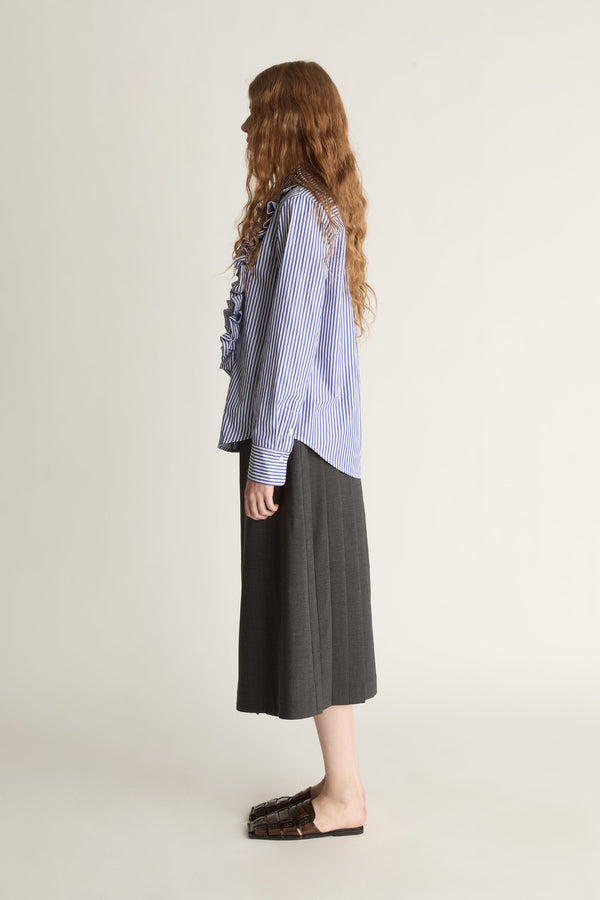 Woman wearing a blue striped shirt with ruffles and a gray skirt on a white background
