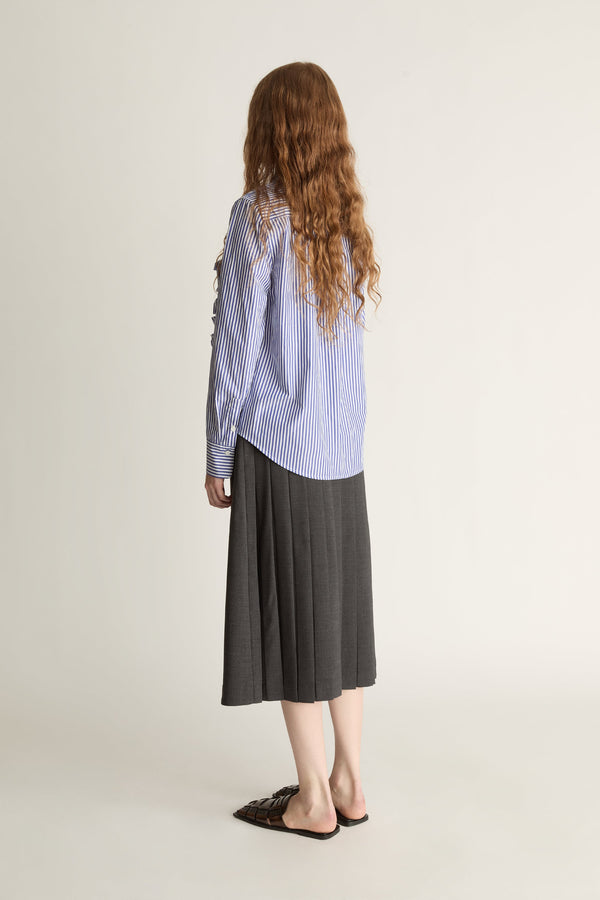 Woman wearing a blue striped shirt with ruffles and a gray skirt on a white background
