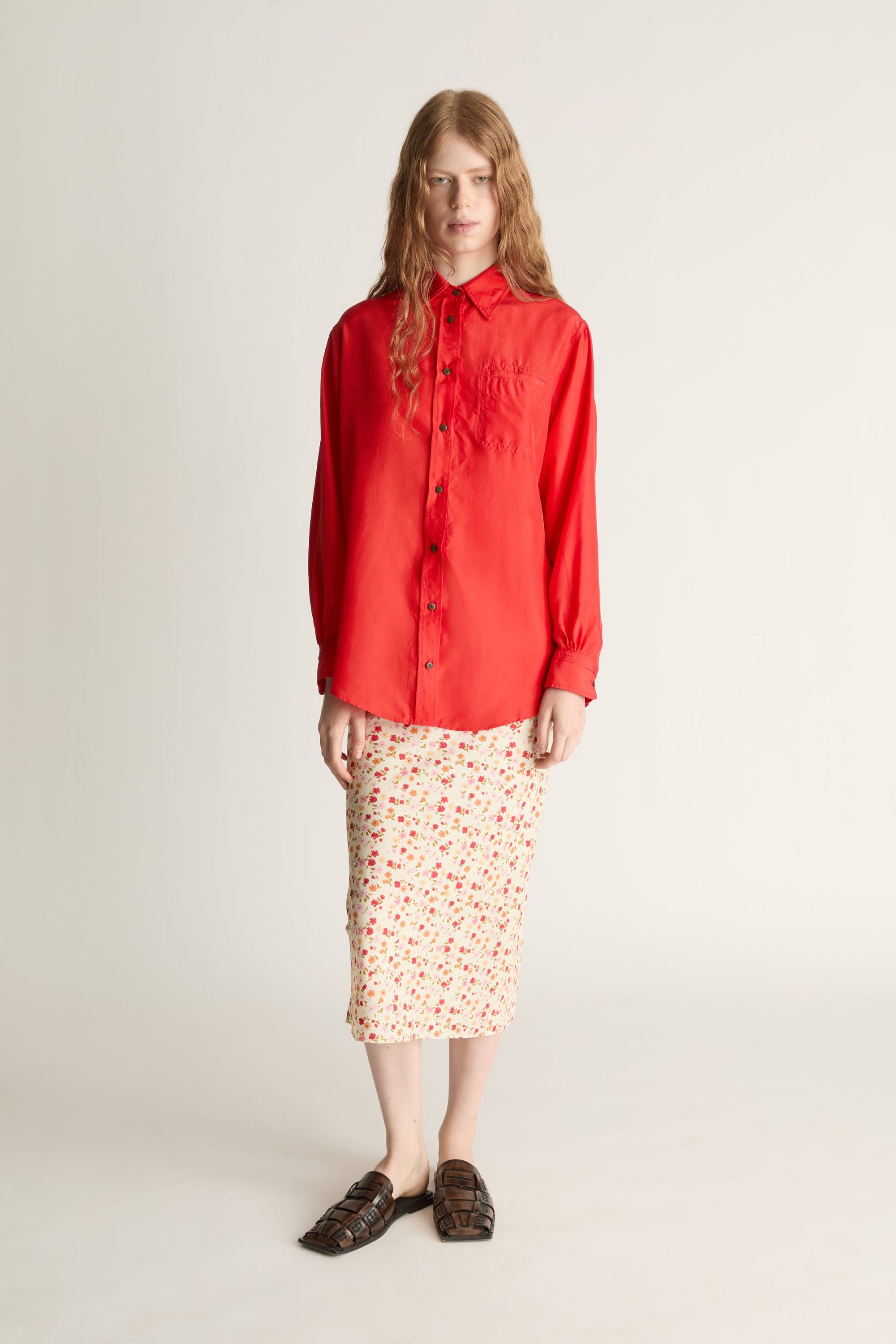 Person wearing a red shirt and patterned skirt on a plain background