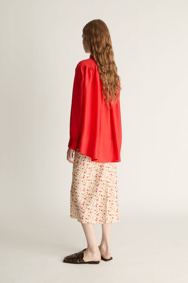 Person wearing a red shirt and patterned skirt on a plain background