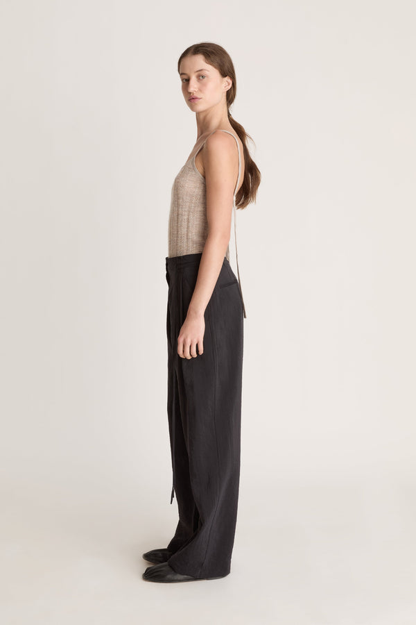 Woman wearing a beige tank top and black pants on a white background