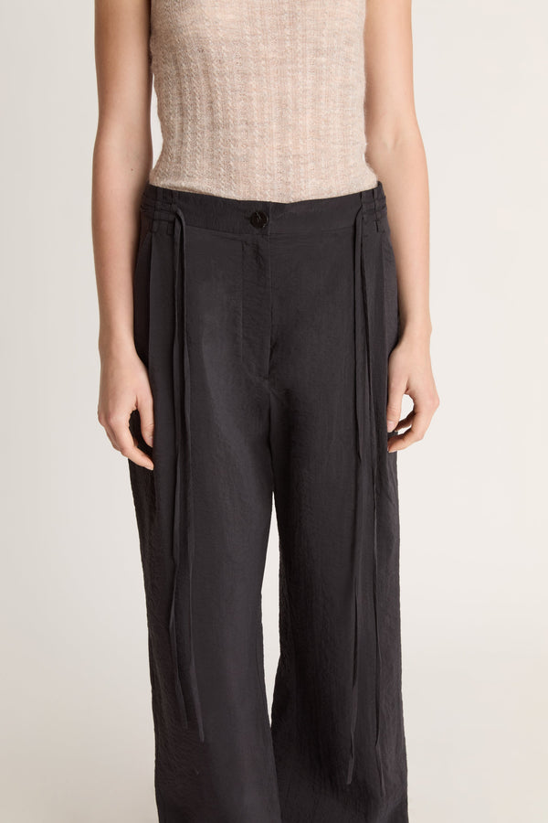 Woman wearing a beige tank top and black pants on a white background