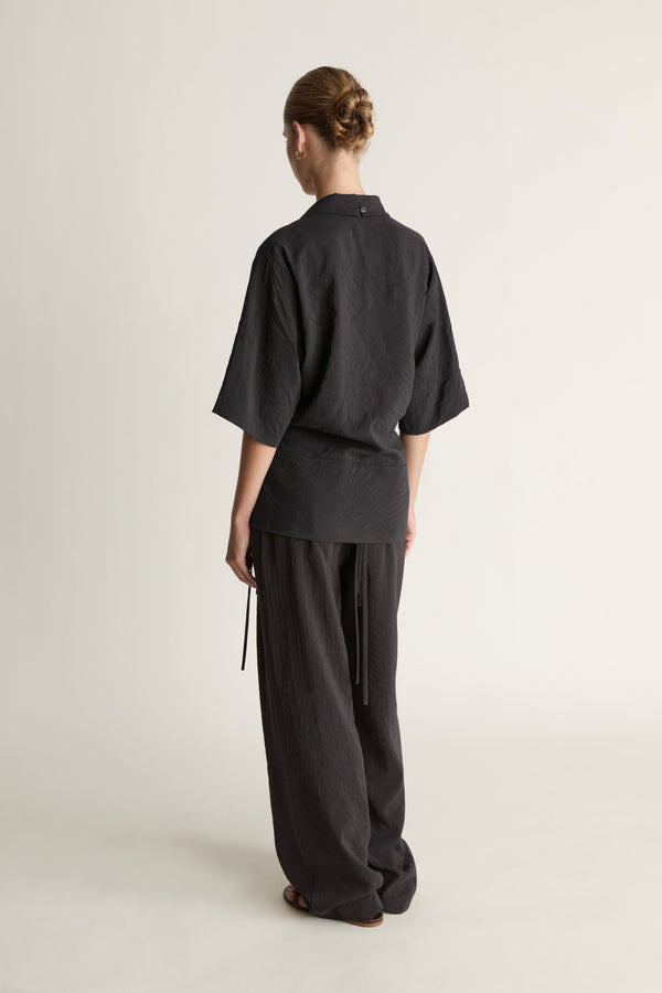 Person wearing a black wrap top with black trousers on a plain background