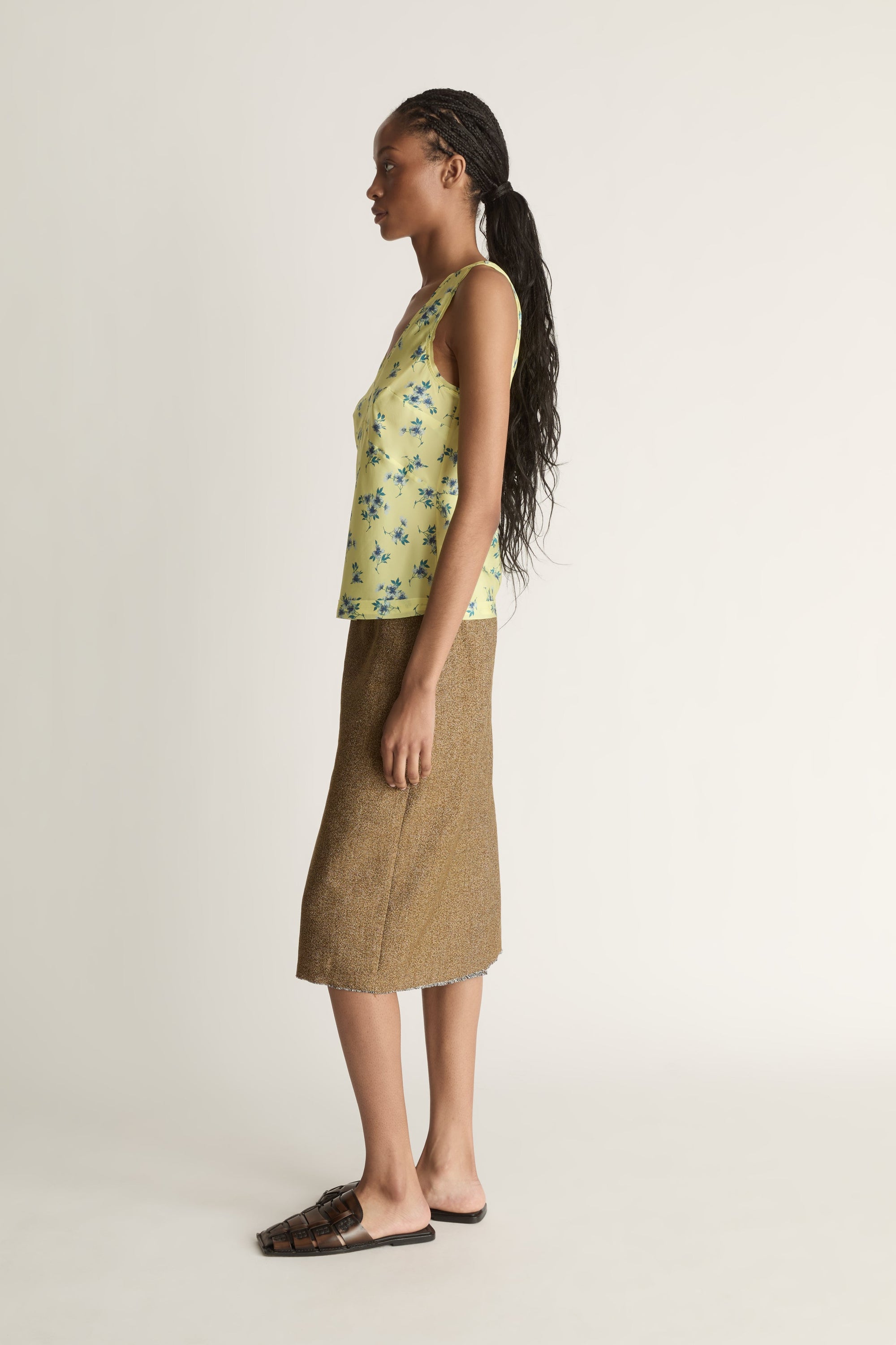 Side view image of a woman wearing the Maisie Silk Cami in Lemon and a nutmeg coloured midi length skirt.