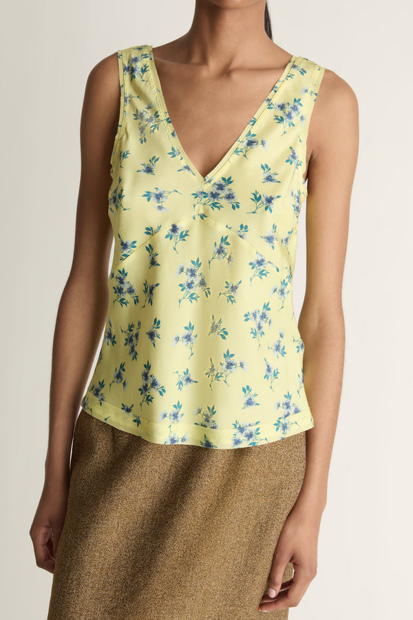 Close-up image of a woman wearing a lemon yellow silk v-neck blouse with blue flowers on it  and a brown skirt