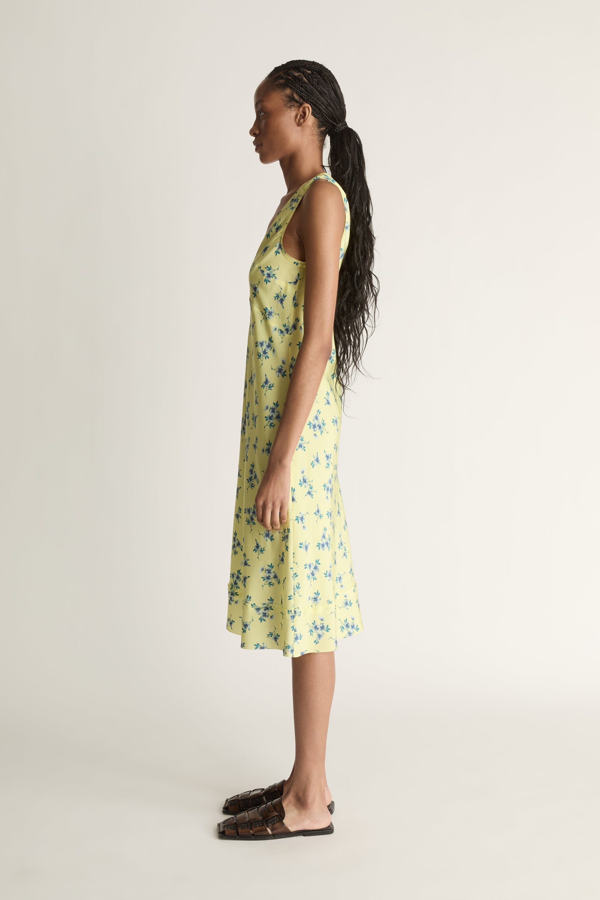 A side view image of a woman wearing a yellow and blue floral print silk slip dress on a white background