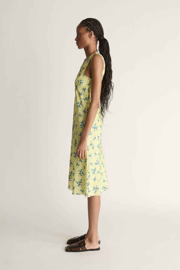 A side view image of a woman wearing a yellow and blue floral print silk slip dress on a white background