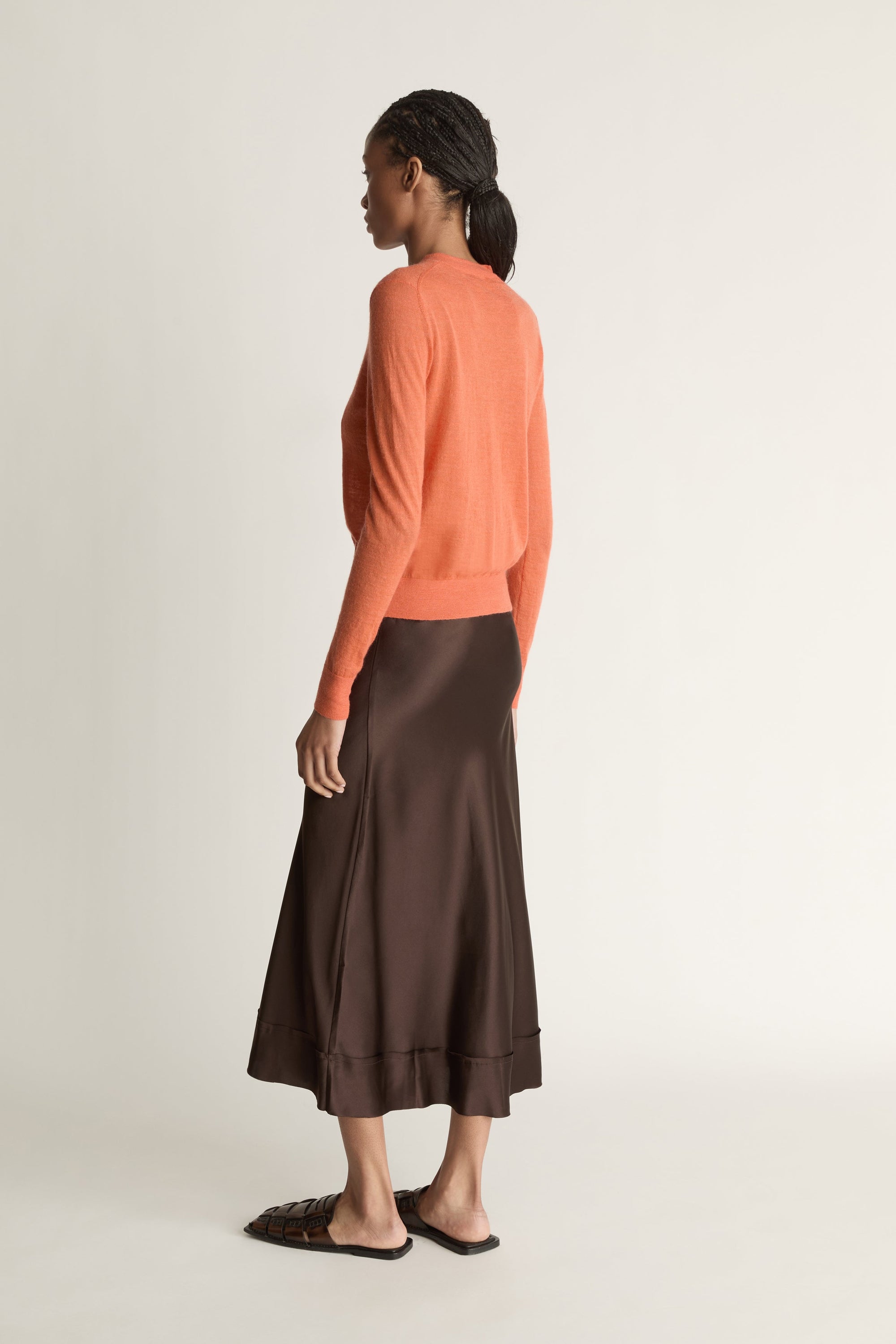 Woman wearing an orange cardigan and brown skirt on a white background
