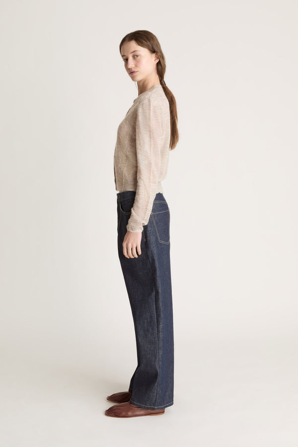 Person wearing a beige cardigan and dark jeans on a white background