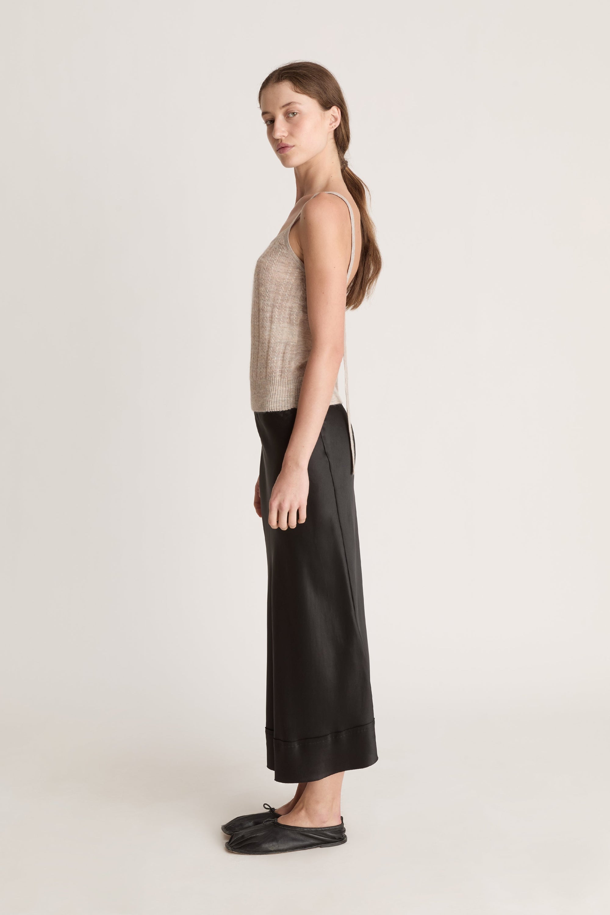 Woman wearing a beige knit cami top and black skirt on a white background
